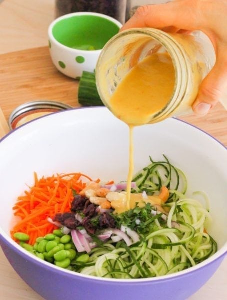 pouring dressing into Mango Curried Cucumber Noodle Salad ingredients